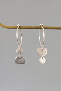 Pair of silver earrings hanging on a branch against a gray background