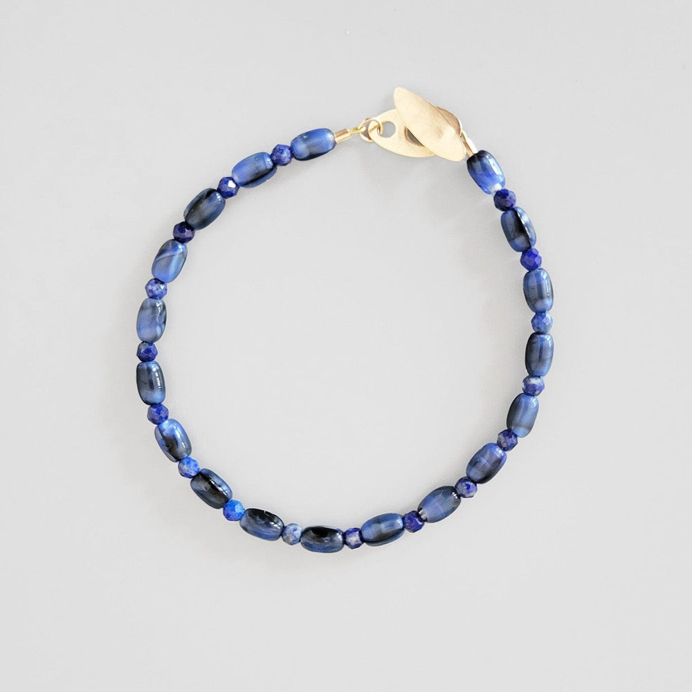 Blue beaded bracelet with a gold clasp on a light gray background