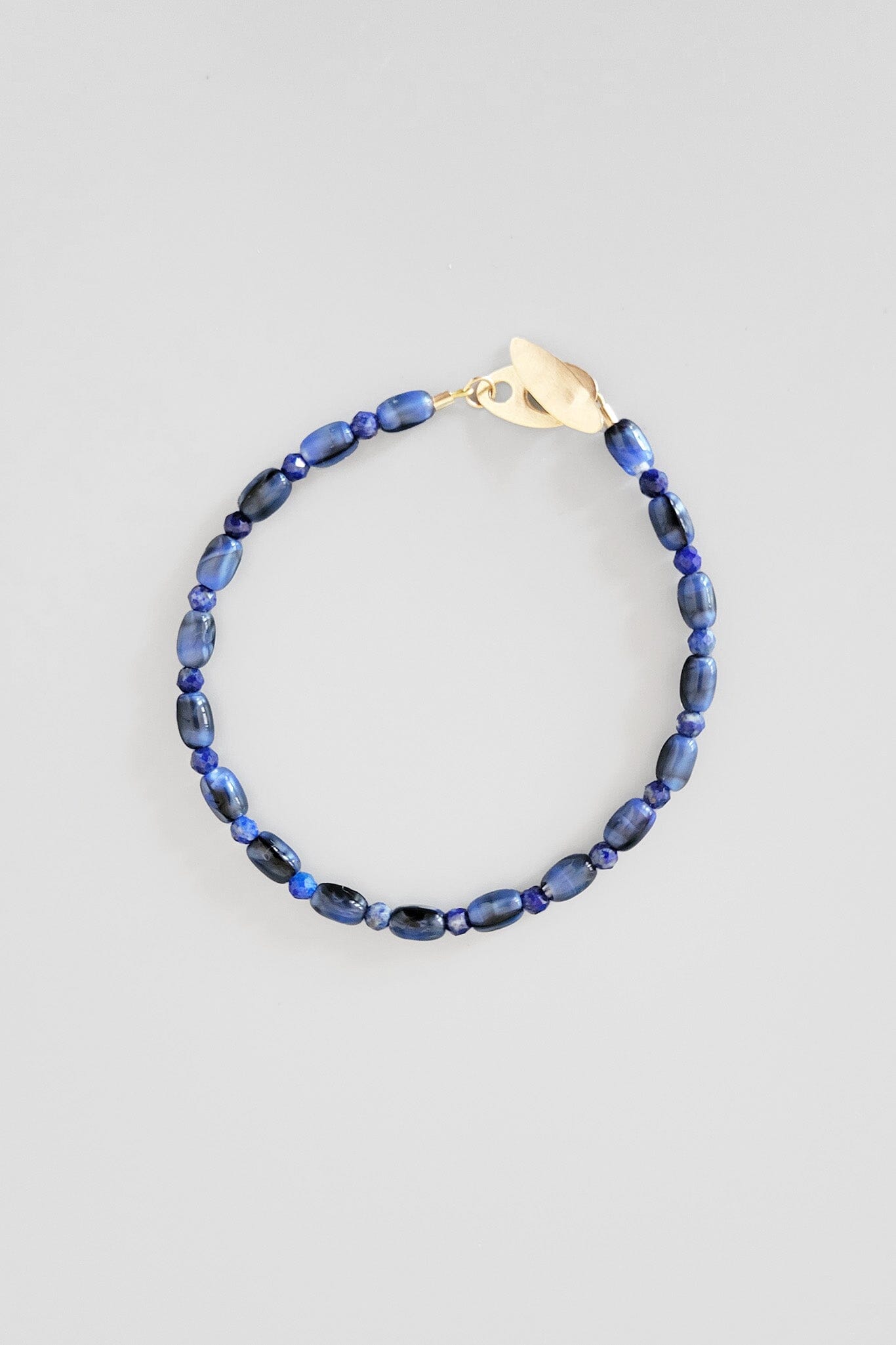 Blue beaded bracelet with a gold clasp on a light gray background