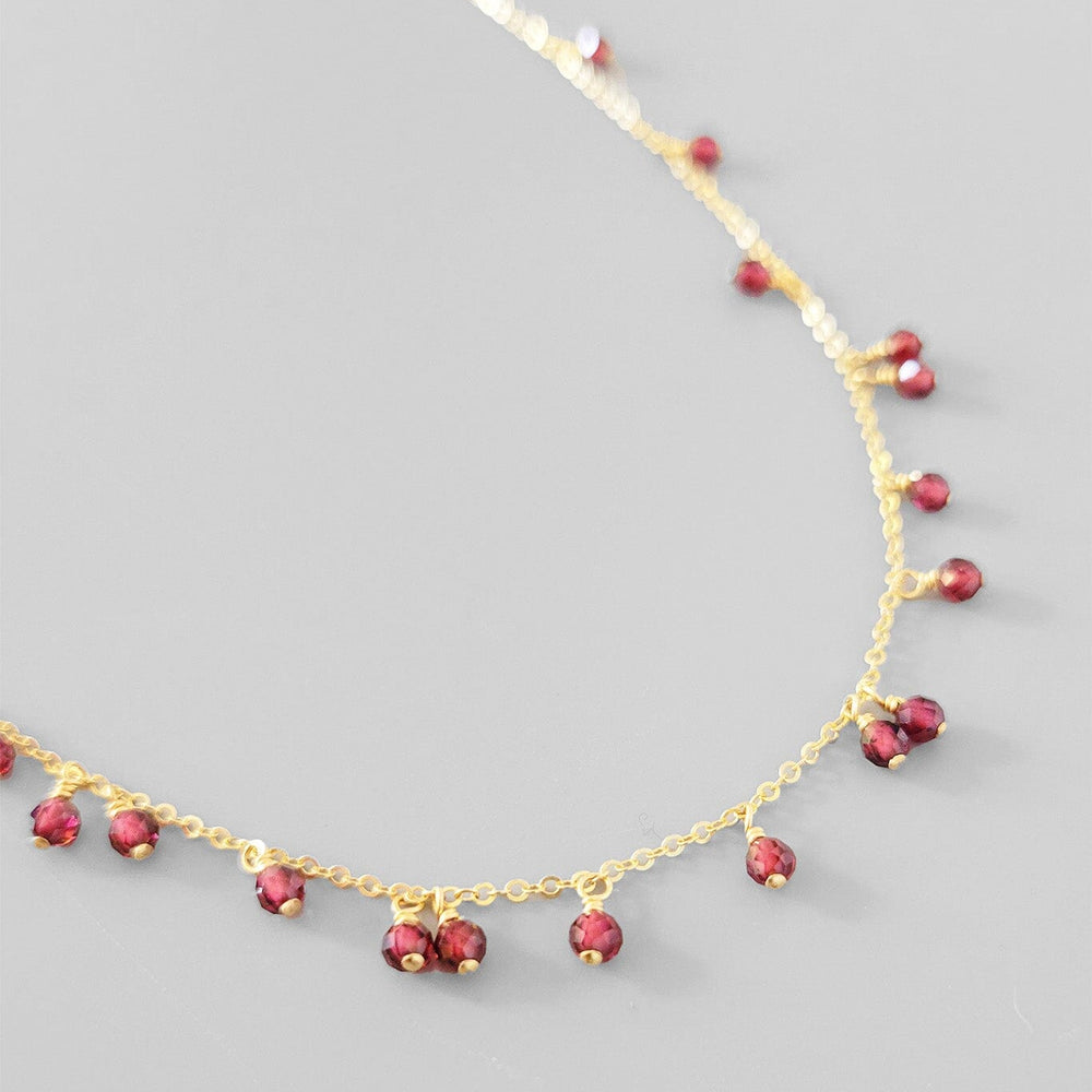 
                  
                    Gold necklace with red gemstones on a gray background
                  
                