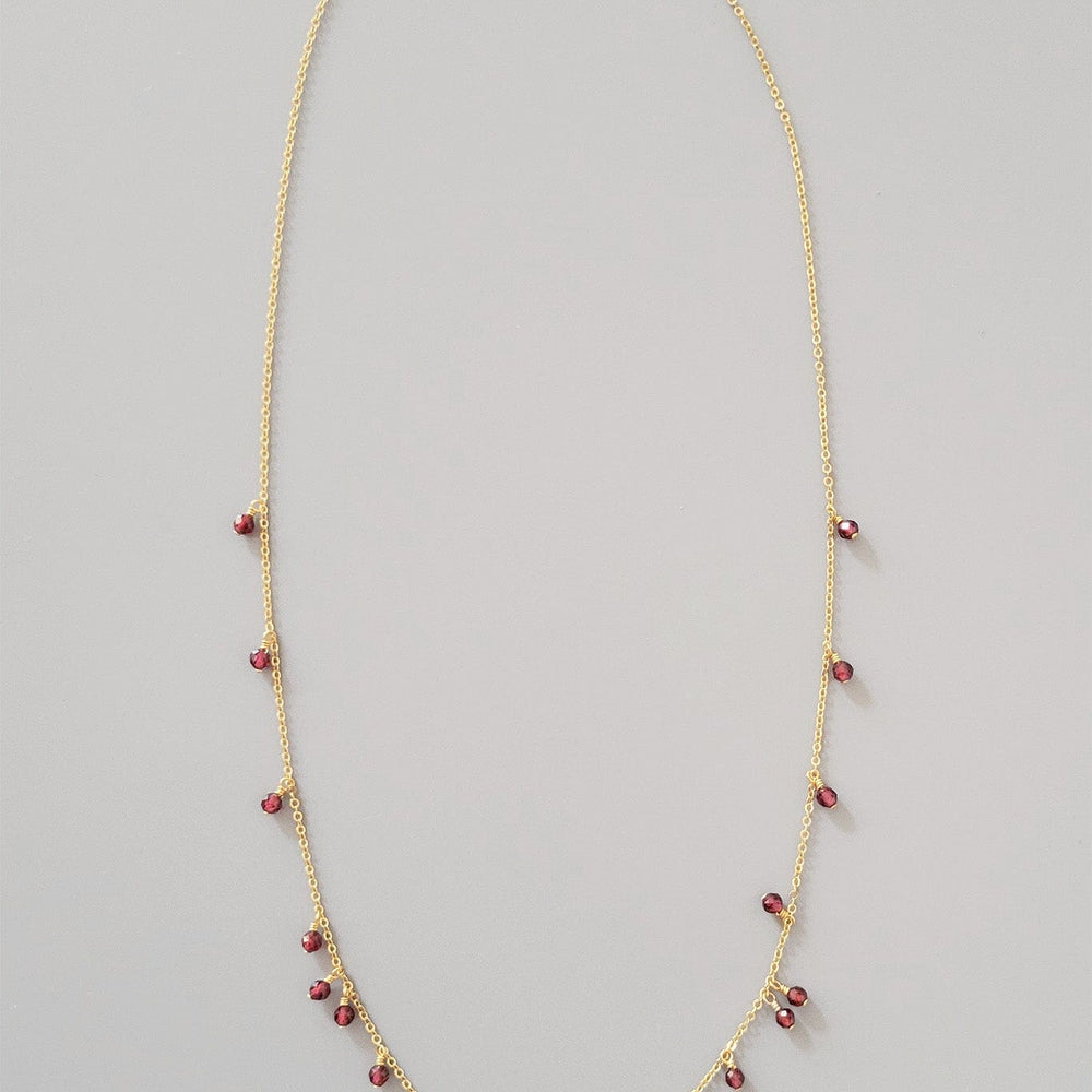 
                  
                    Gold necklace with red beads on a gray background
                  
                