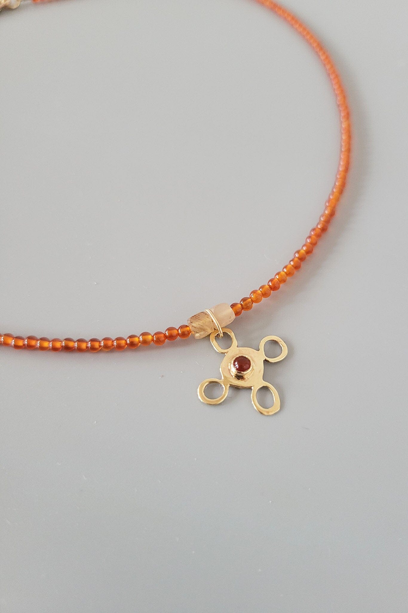 Necklace with orange beads and a gold pendant on a gray background
