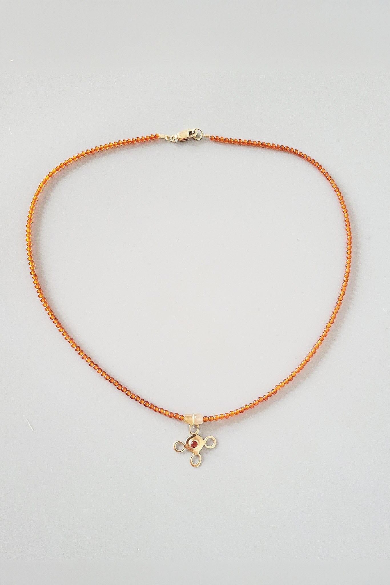 Orange beaded necklace with a small pendant on a light gray background