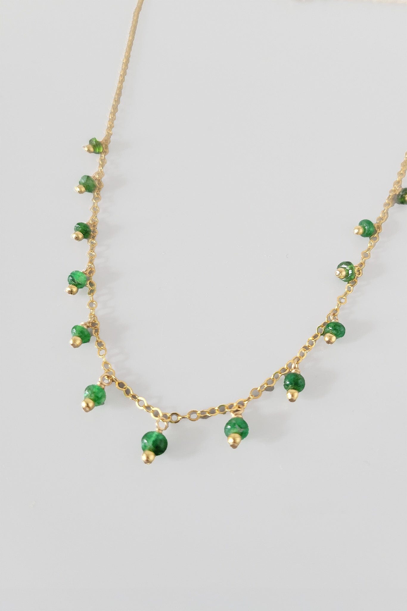 Gold necklace with green gemstones on a light gray background