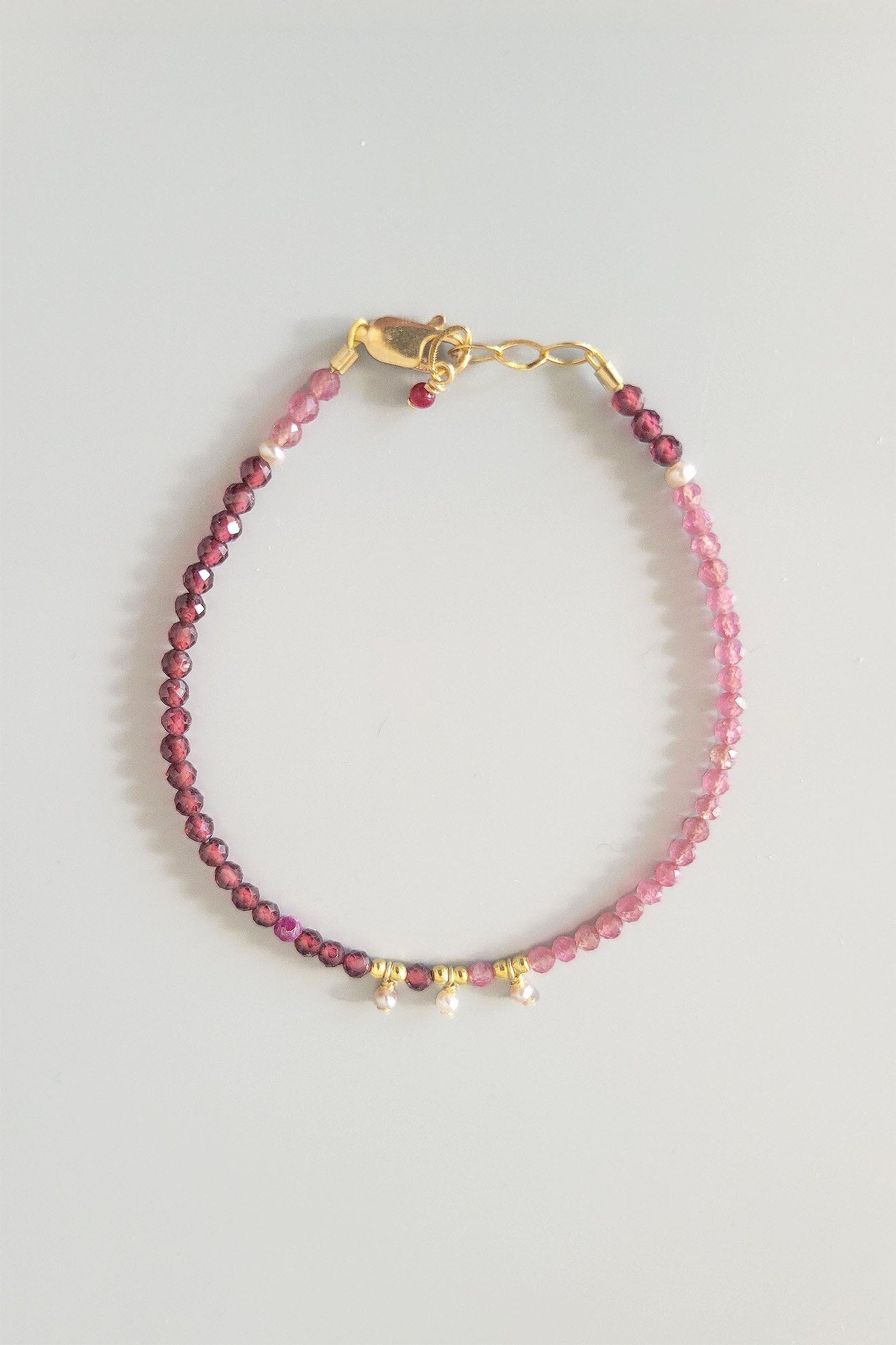 Pink beaded tourmaline bracelet with gold accents on a light gray background