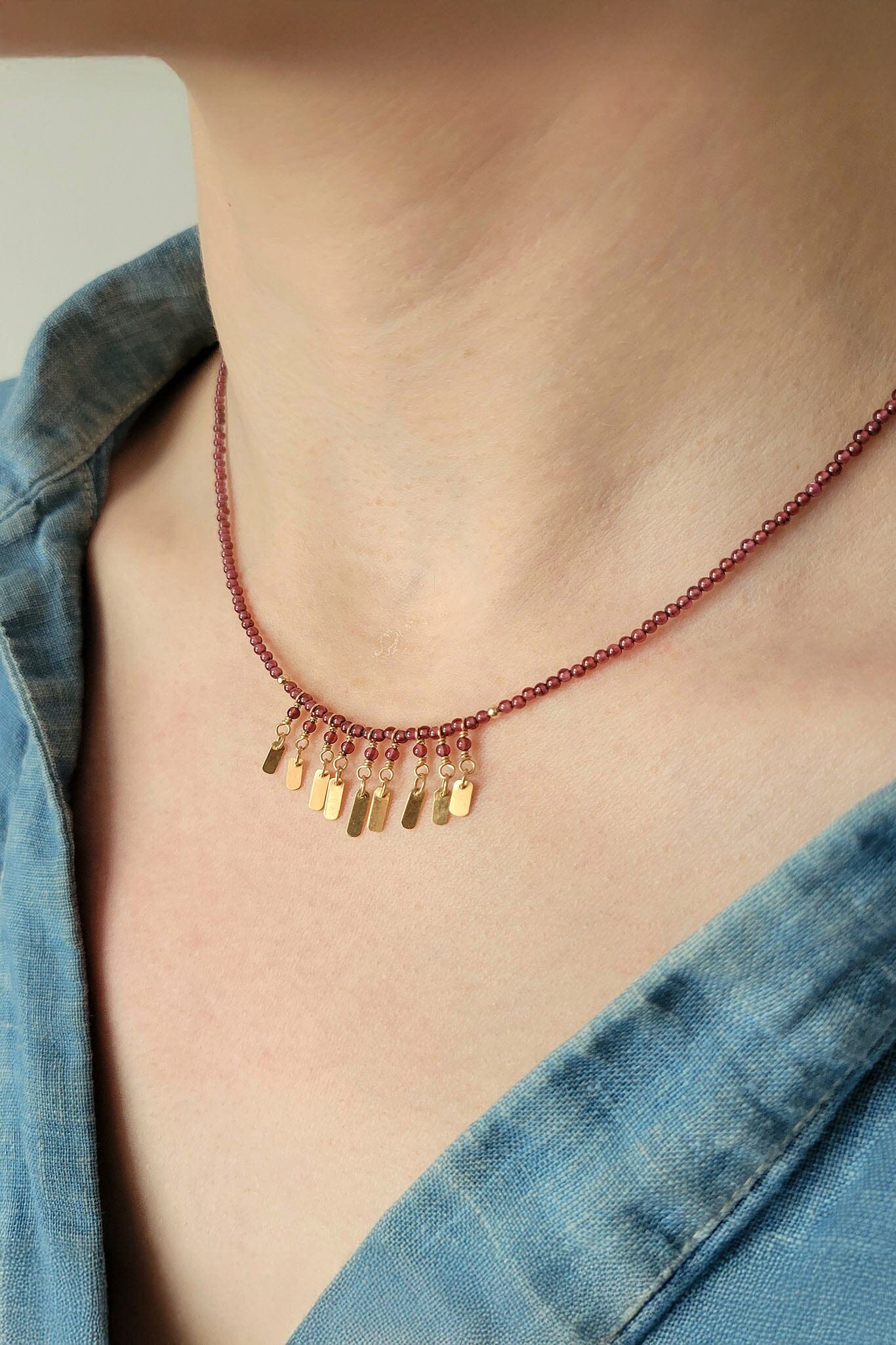 Necklace with gold pendants on a person wearing a blue denim shirt.