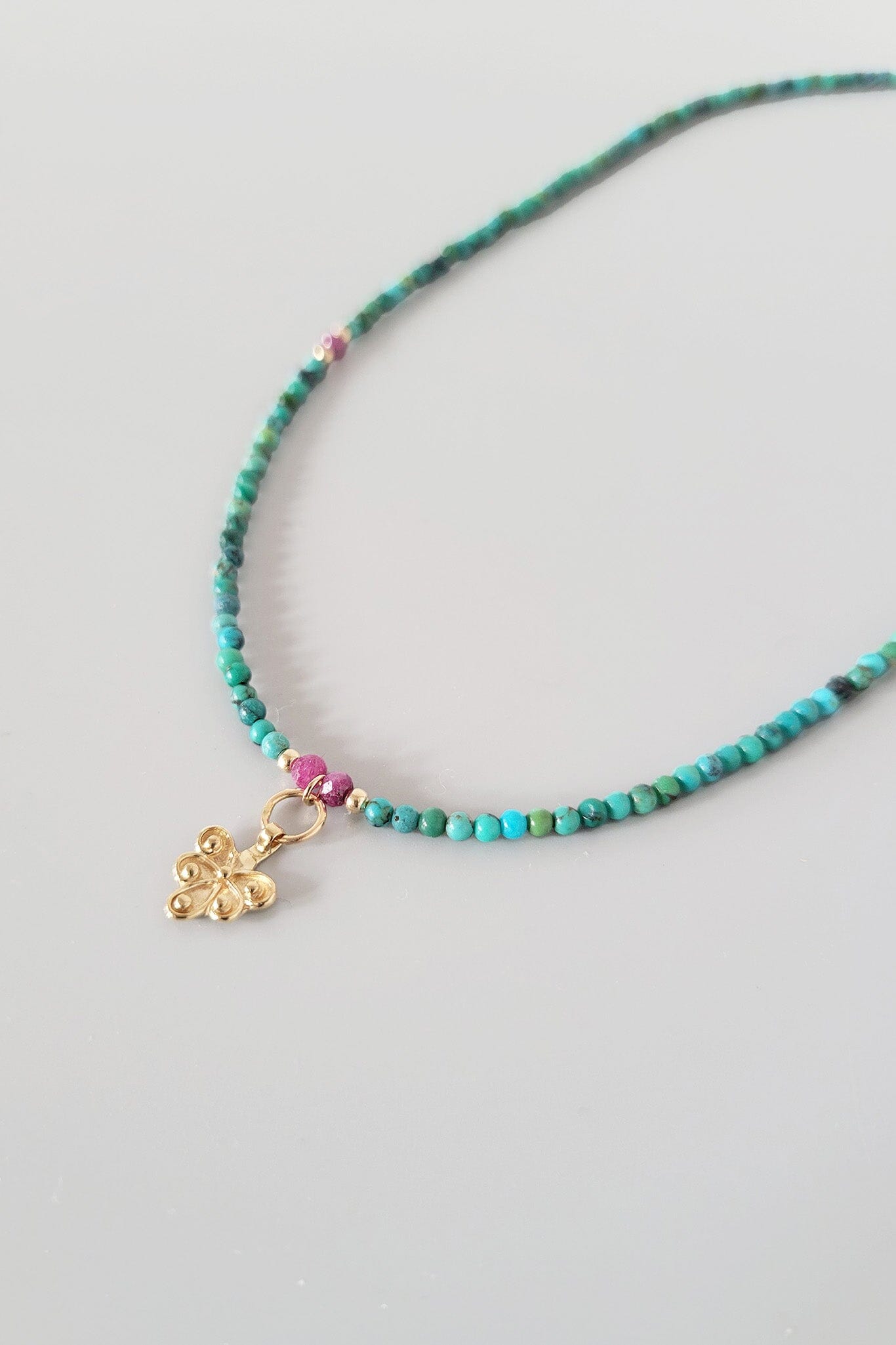 Necklace with turquoise beads and a gold charm on a light gray background