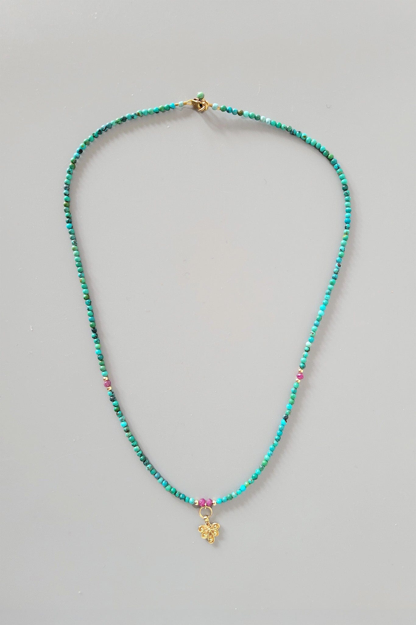 Turquoise beaded necklace with a small charm on a gray background