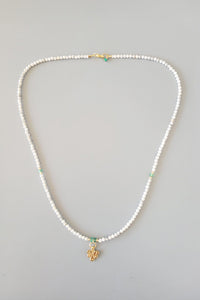 Pearl necklace with a small gold charm on a gray background