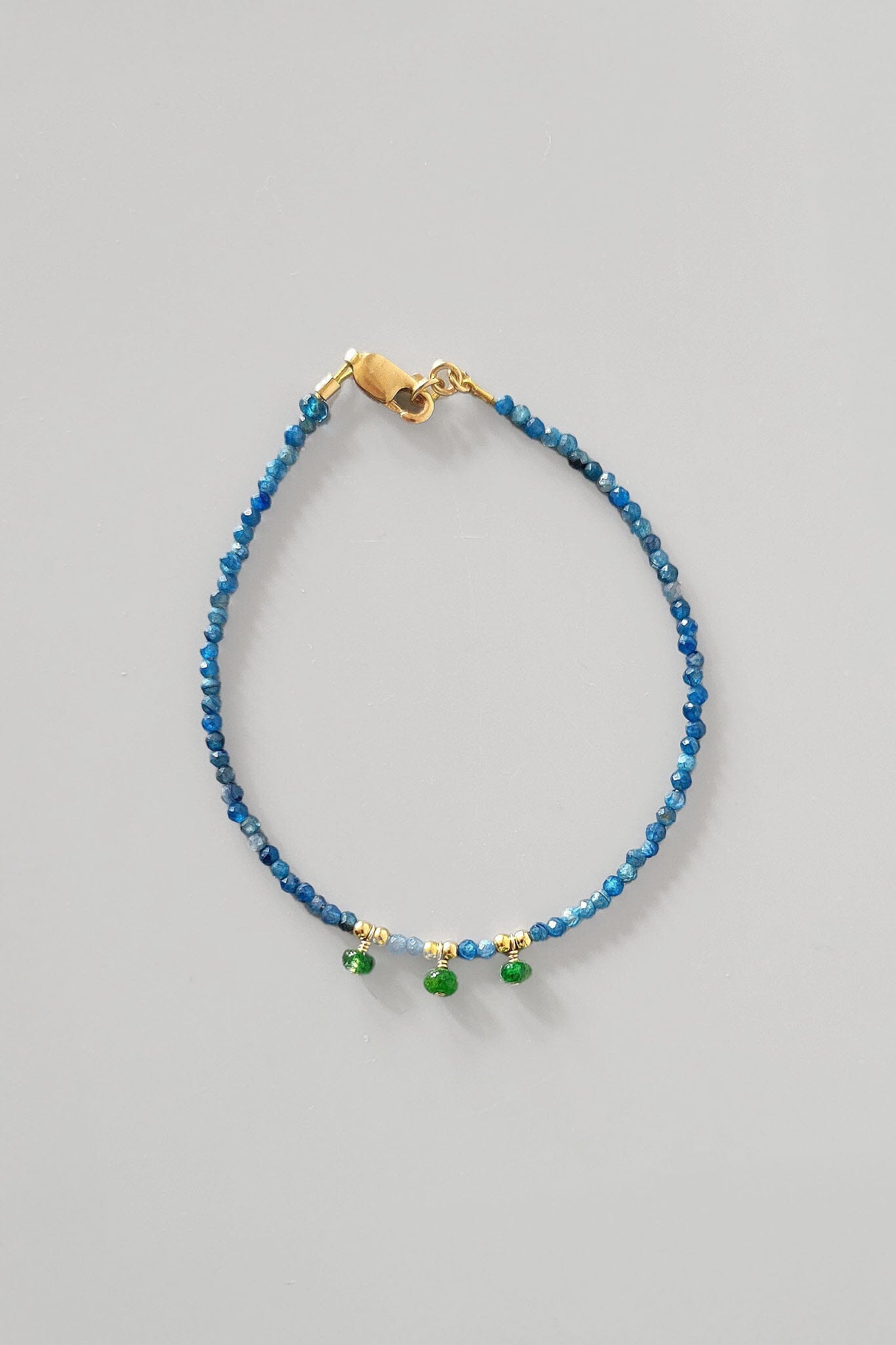 Blue beaded bracelet with gold clasp on a gray background