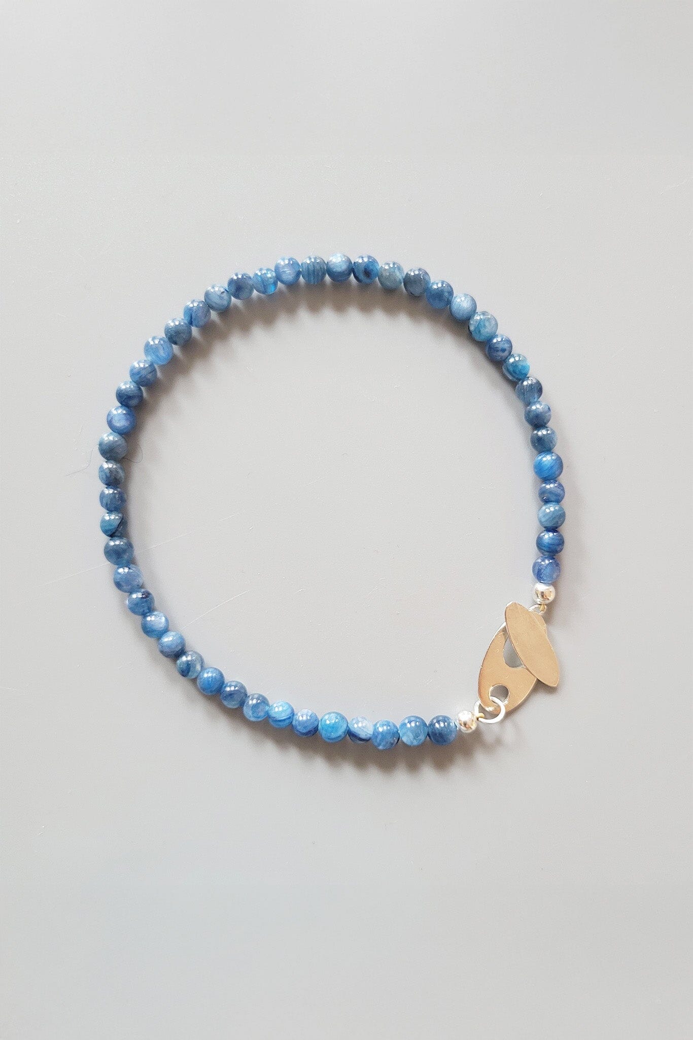 Blue beaded bracelet with a gold charm on a light gray background