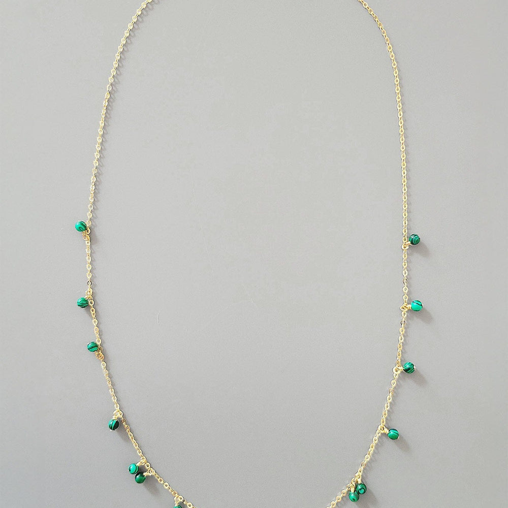 Gold necklace with green beads on a gray background