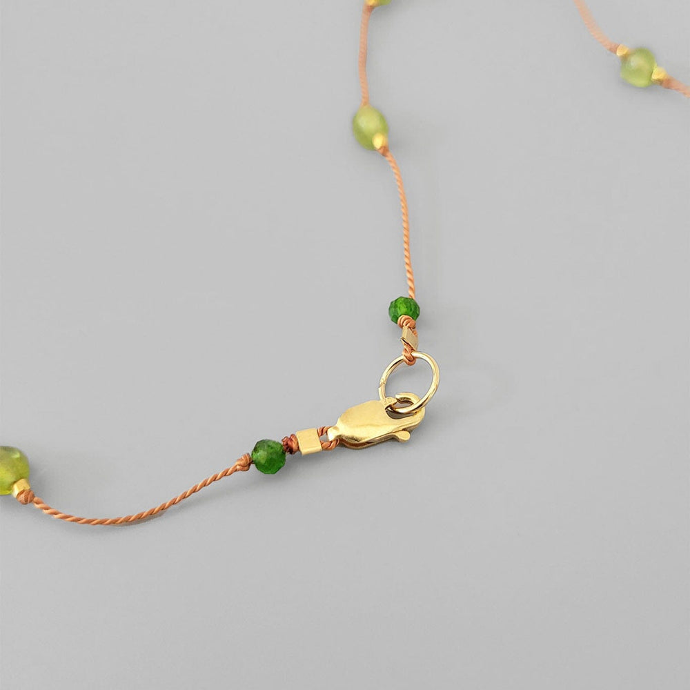 
                  
                    Necklace with green beads and a gold clasp on a gray background
                  
                