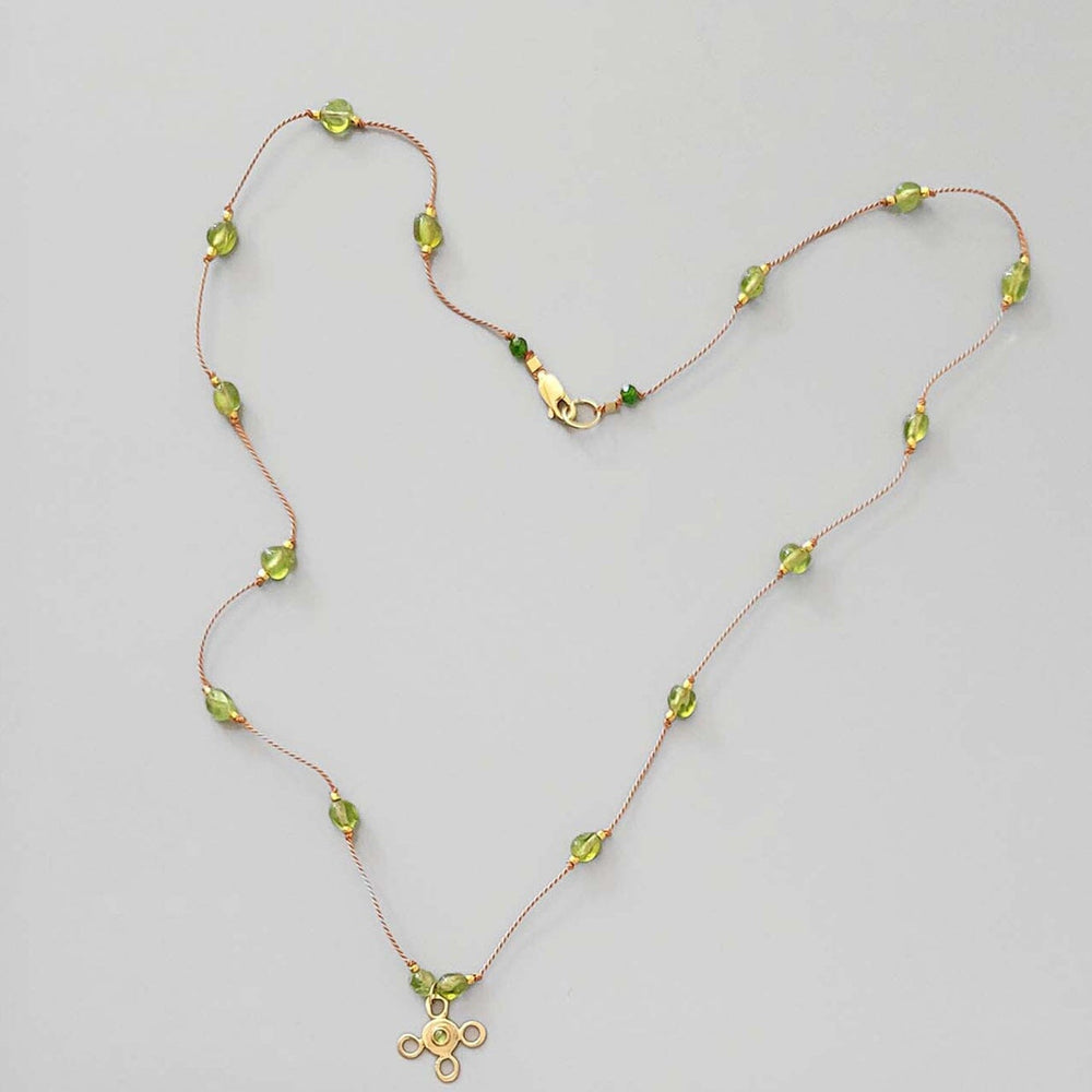 
                  
                    Necklace with green peridot beads and gold pendent on a gray background
                  
                