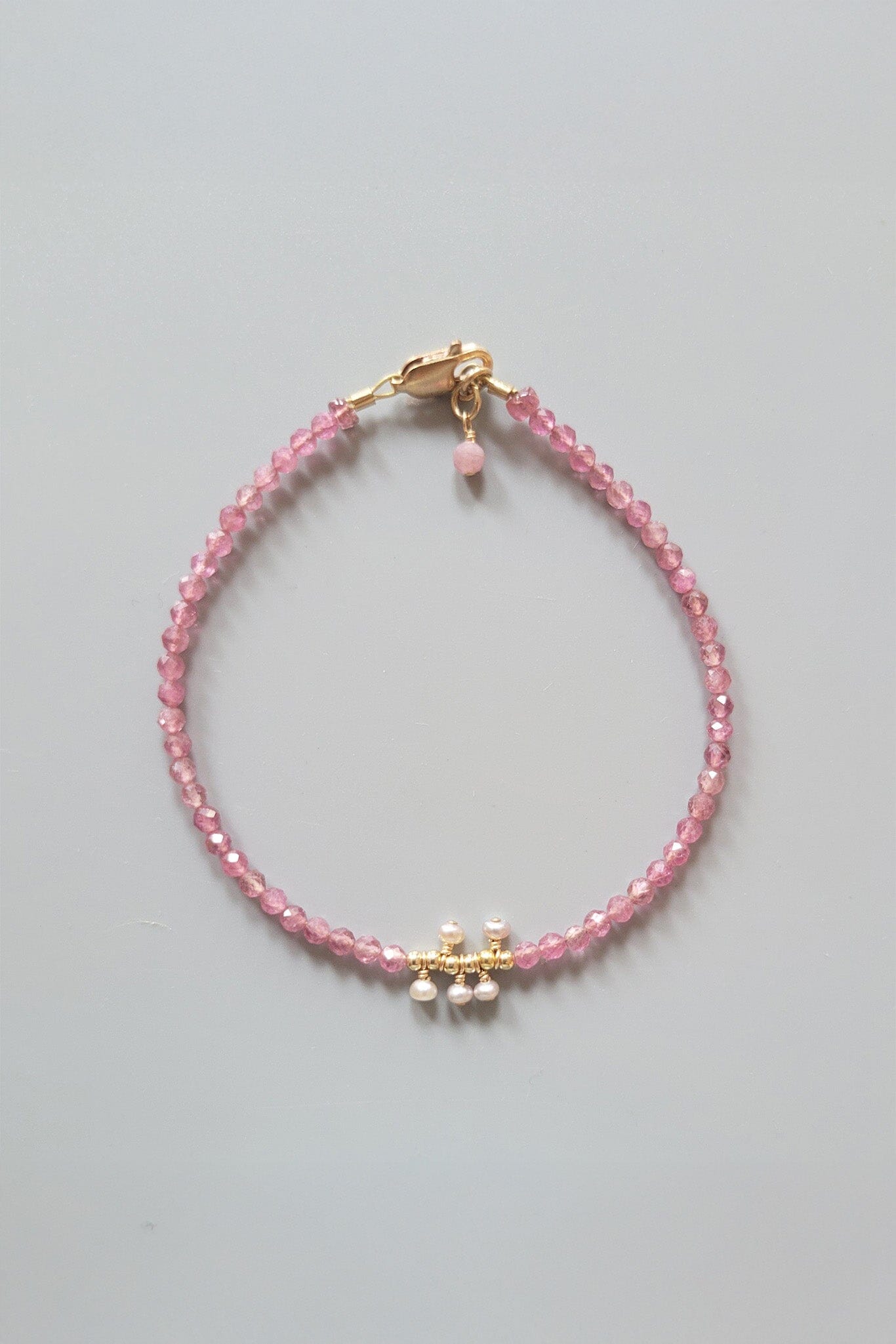 Pink beaded bracelet with a gold clasp on a gray background