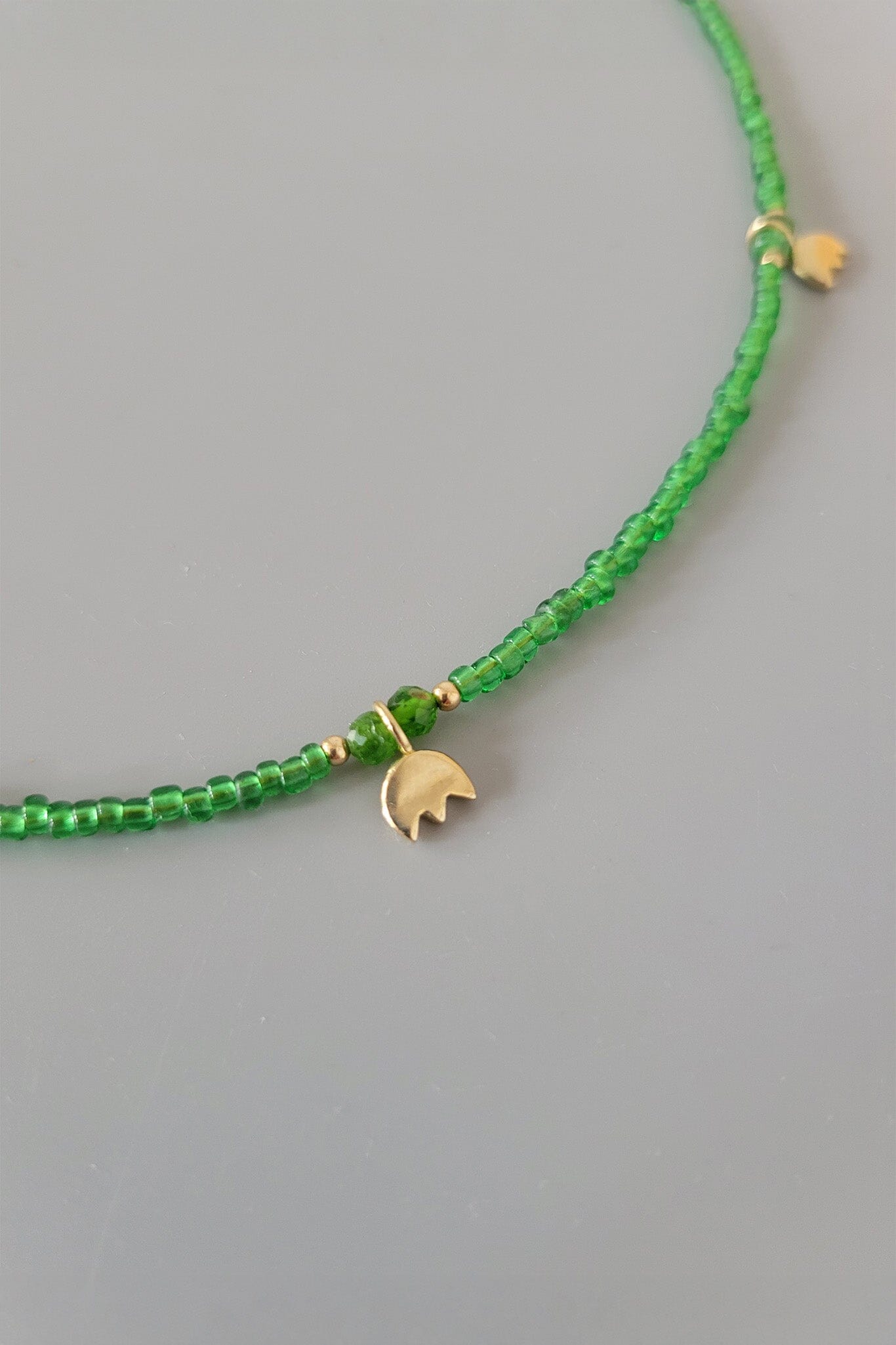Green beaded bracelet with a gold charm on a gray background
