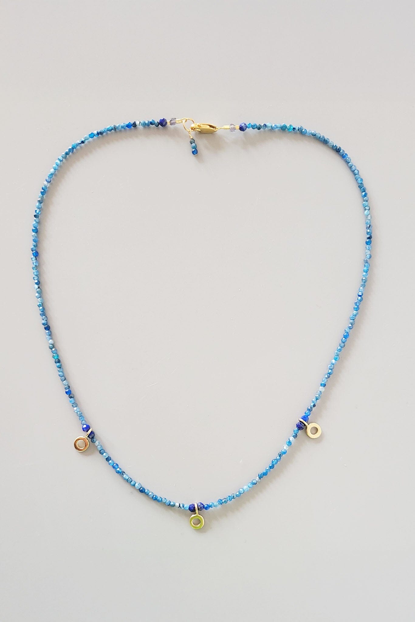 Blue beaded necklace with gold accents on a light gray background