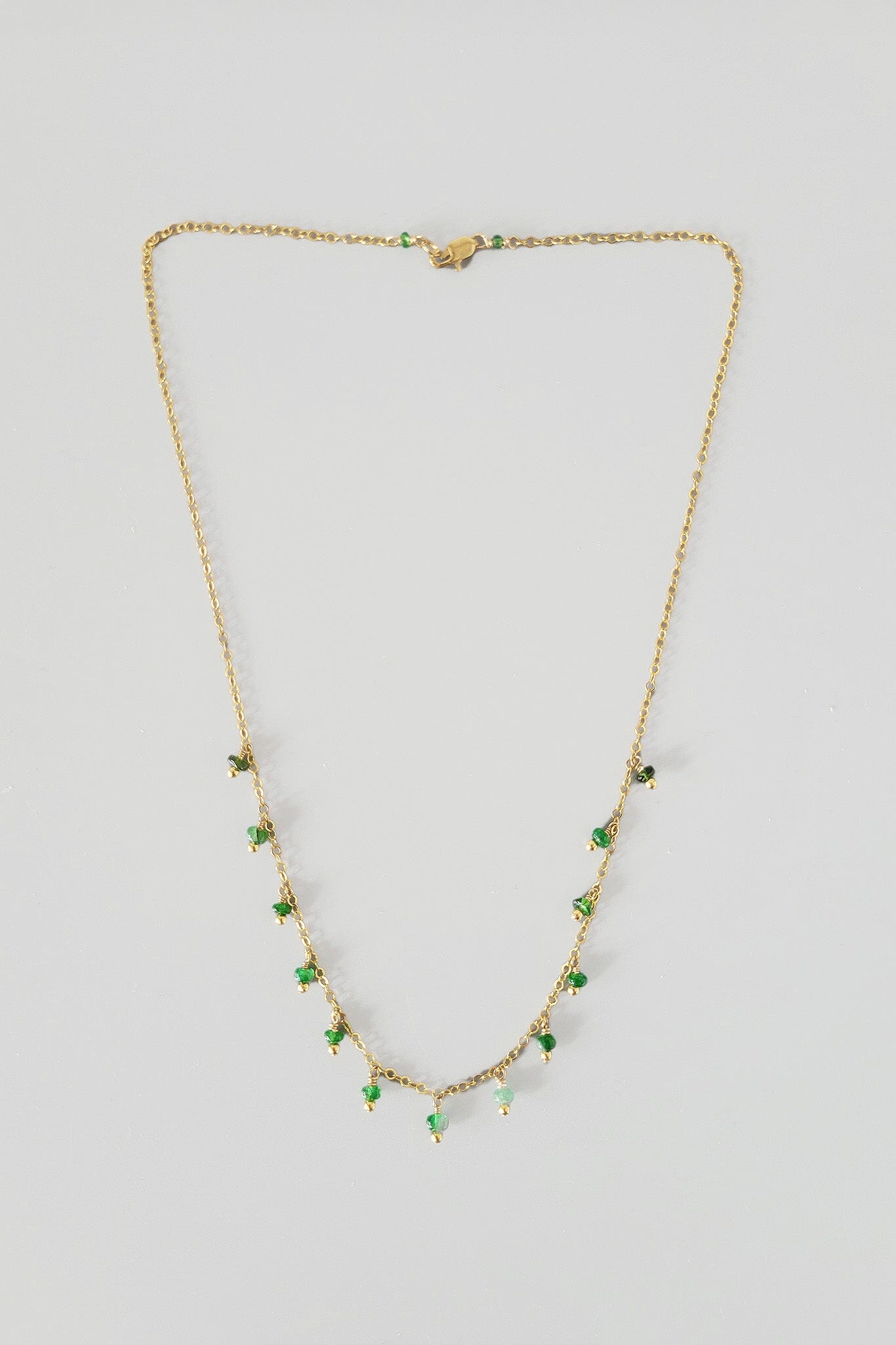 Gold necklace with emerald gemstones on a light gray background