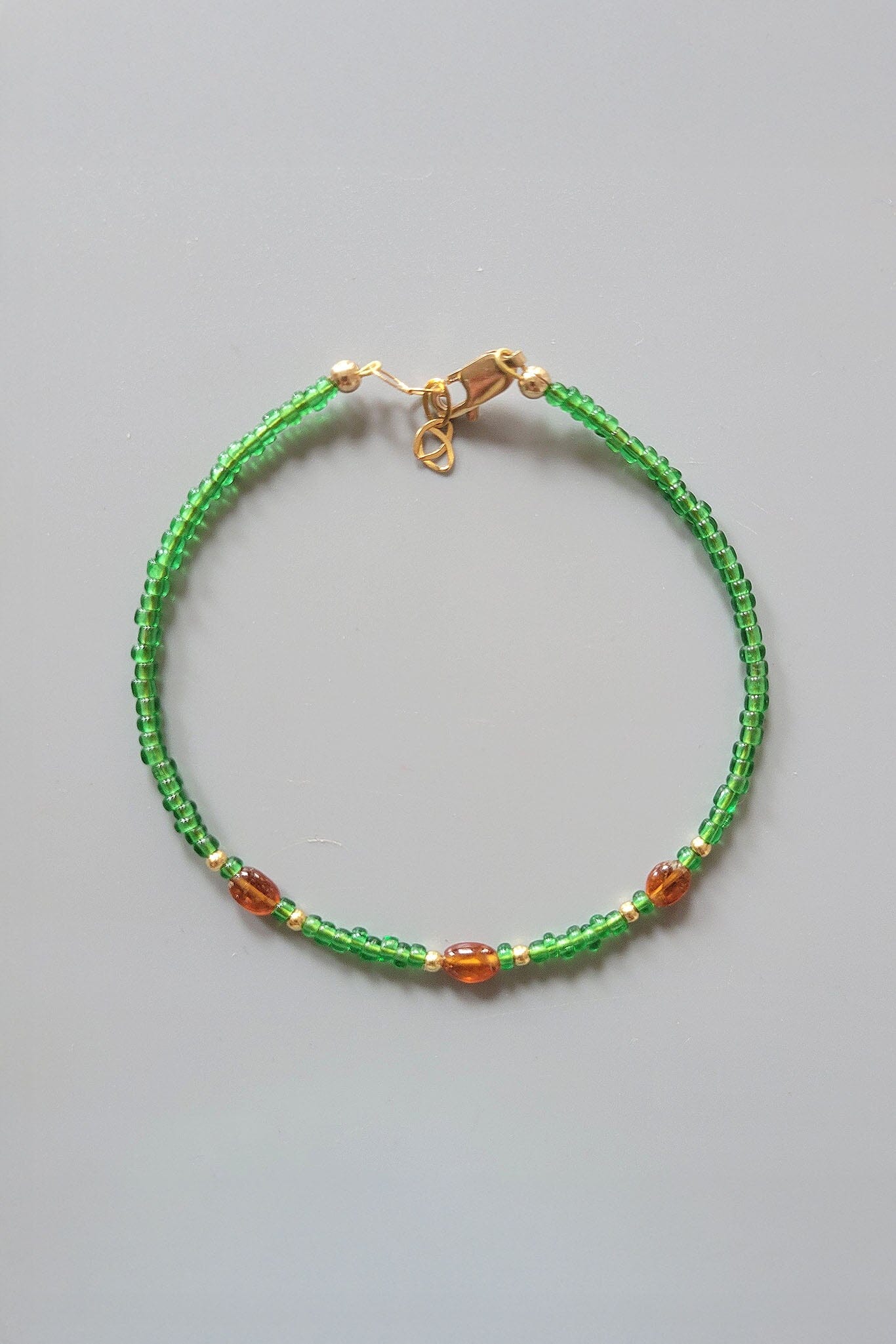 Green beaded bracelet with gold clasp on a gray background