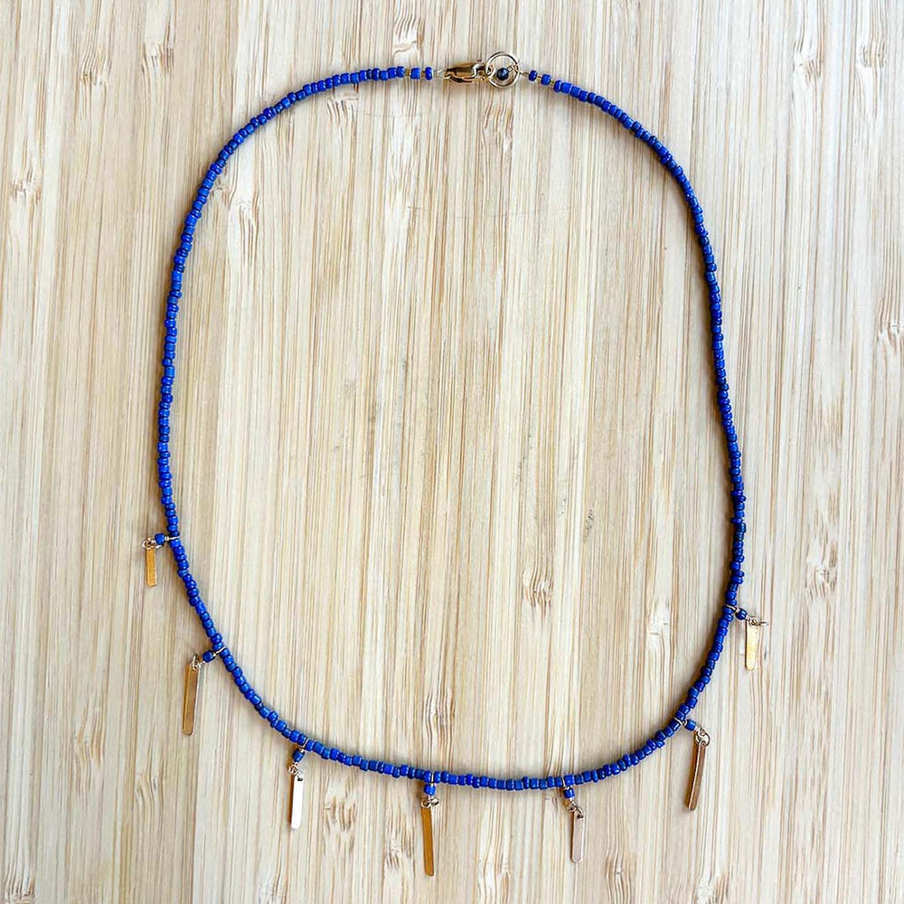 Blue beaded necklace with gold tassel beads on a wooden surface