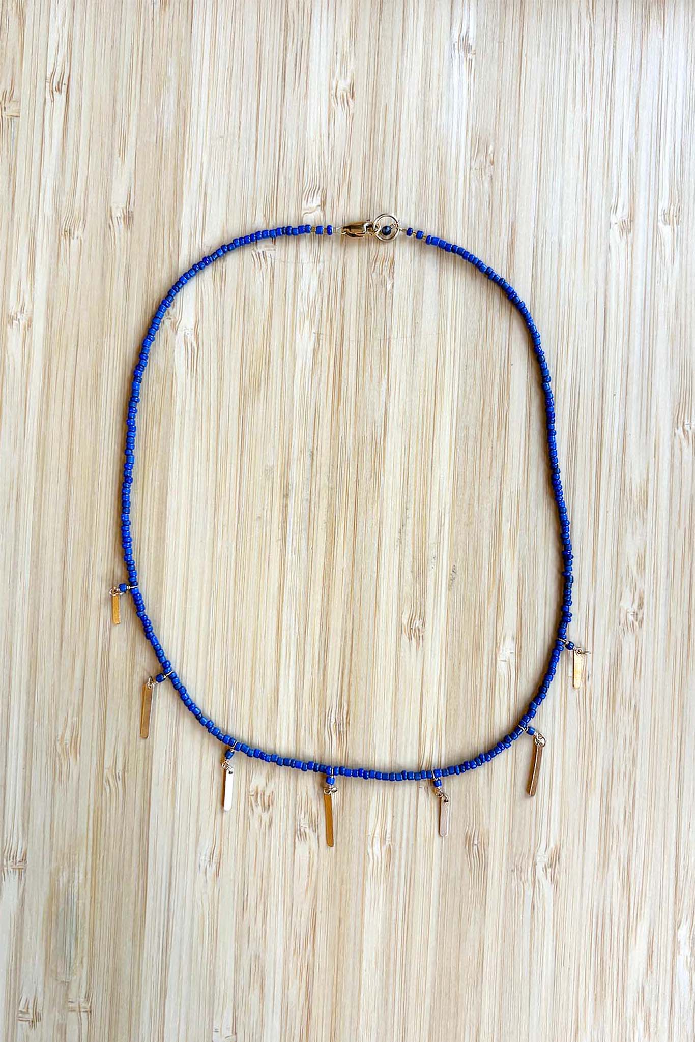 Blue beaded necklace with gold tassel beads on a wooden surface