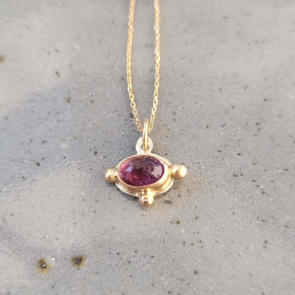 Gold necklace with an oval pink tourmaline gemstone pendant on a neutral background.