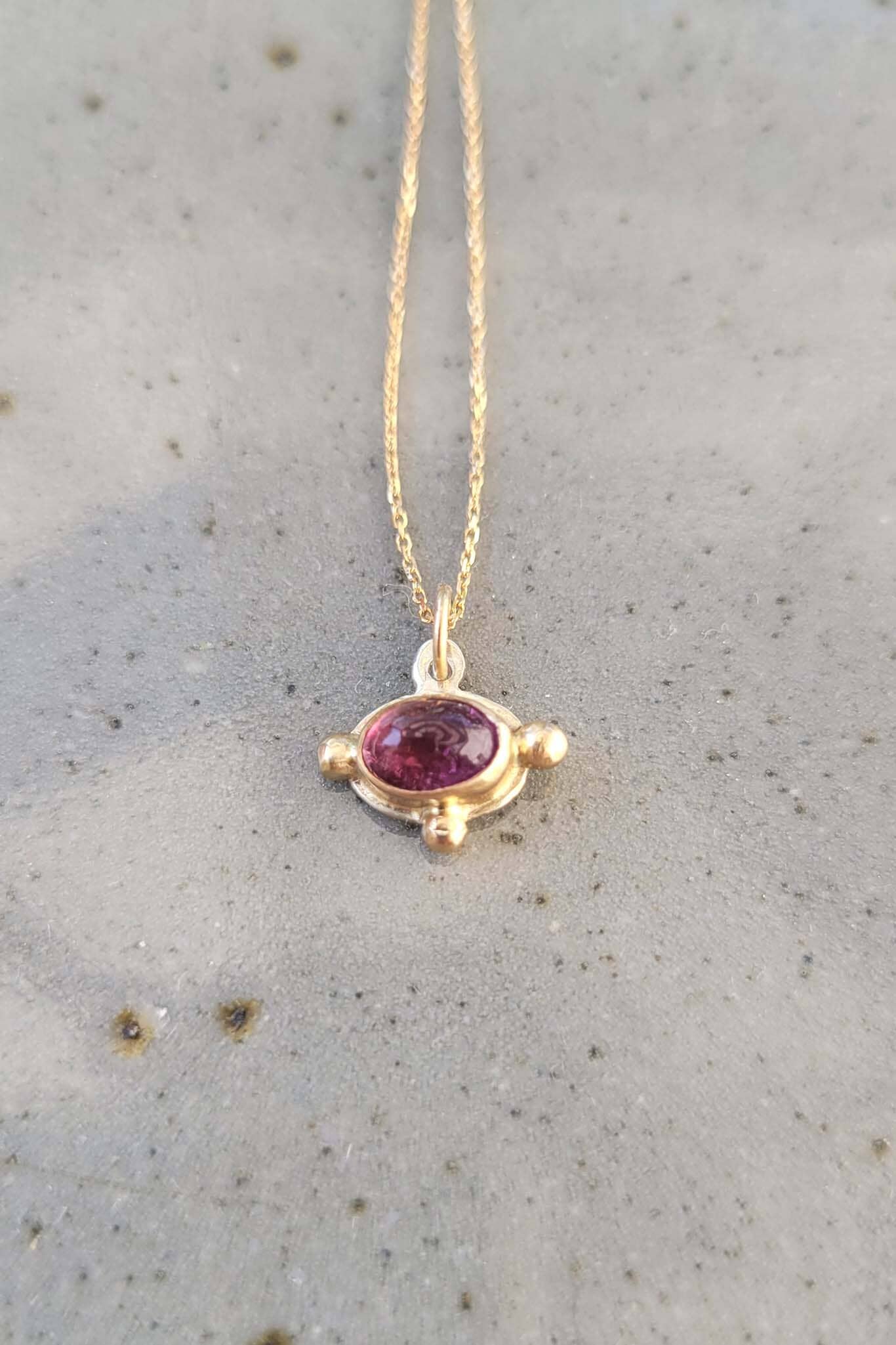 Gold necklace with an oval pink tourmaline gemstone pendant on a neutral background.