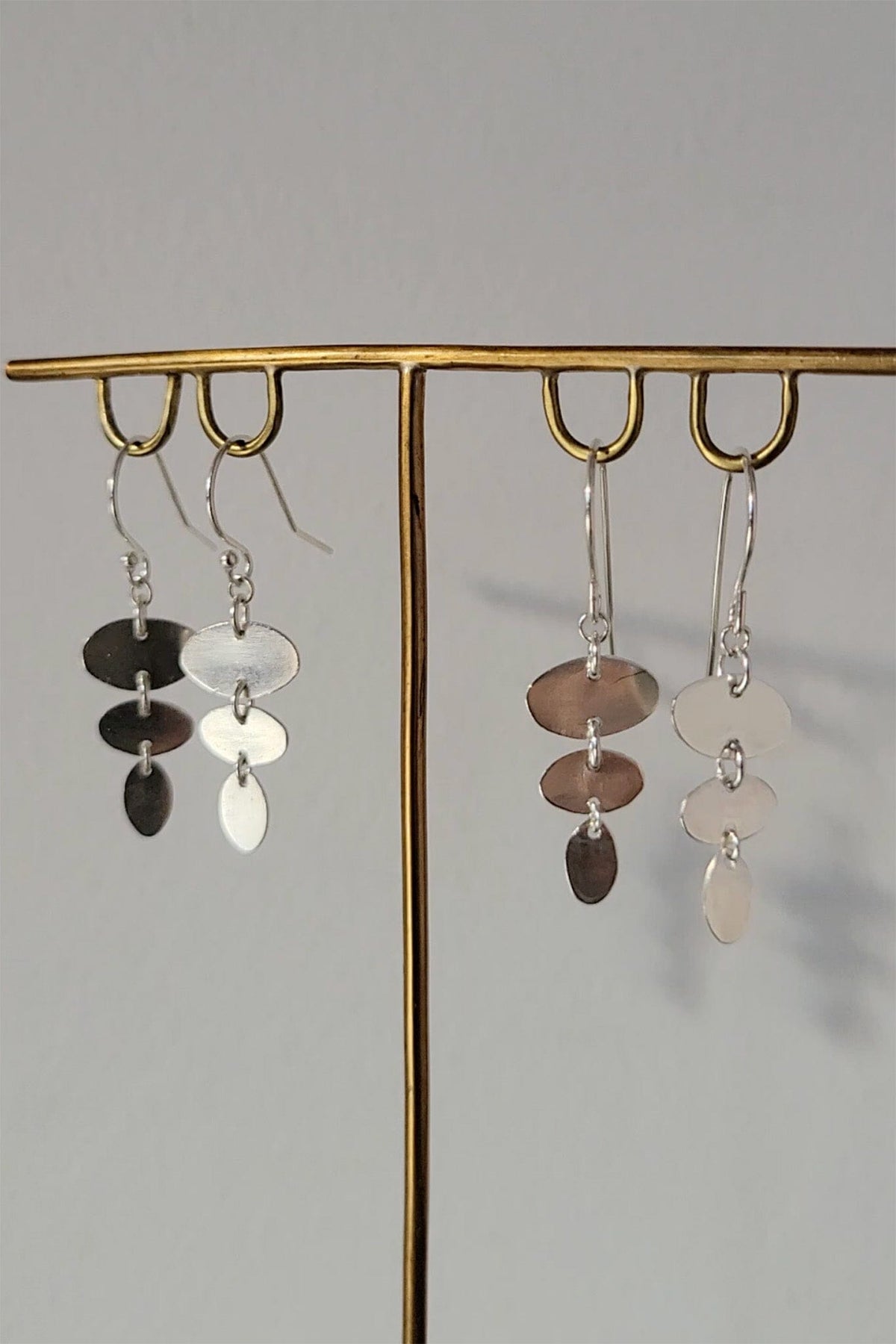 Pair of dangling earrings on a gold stand against a gray background