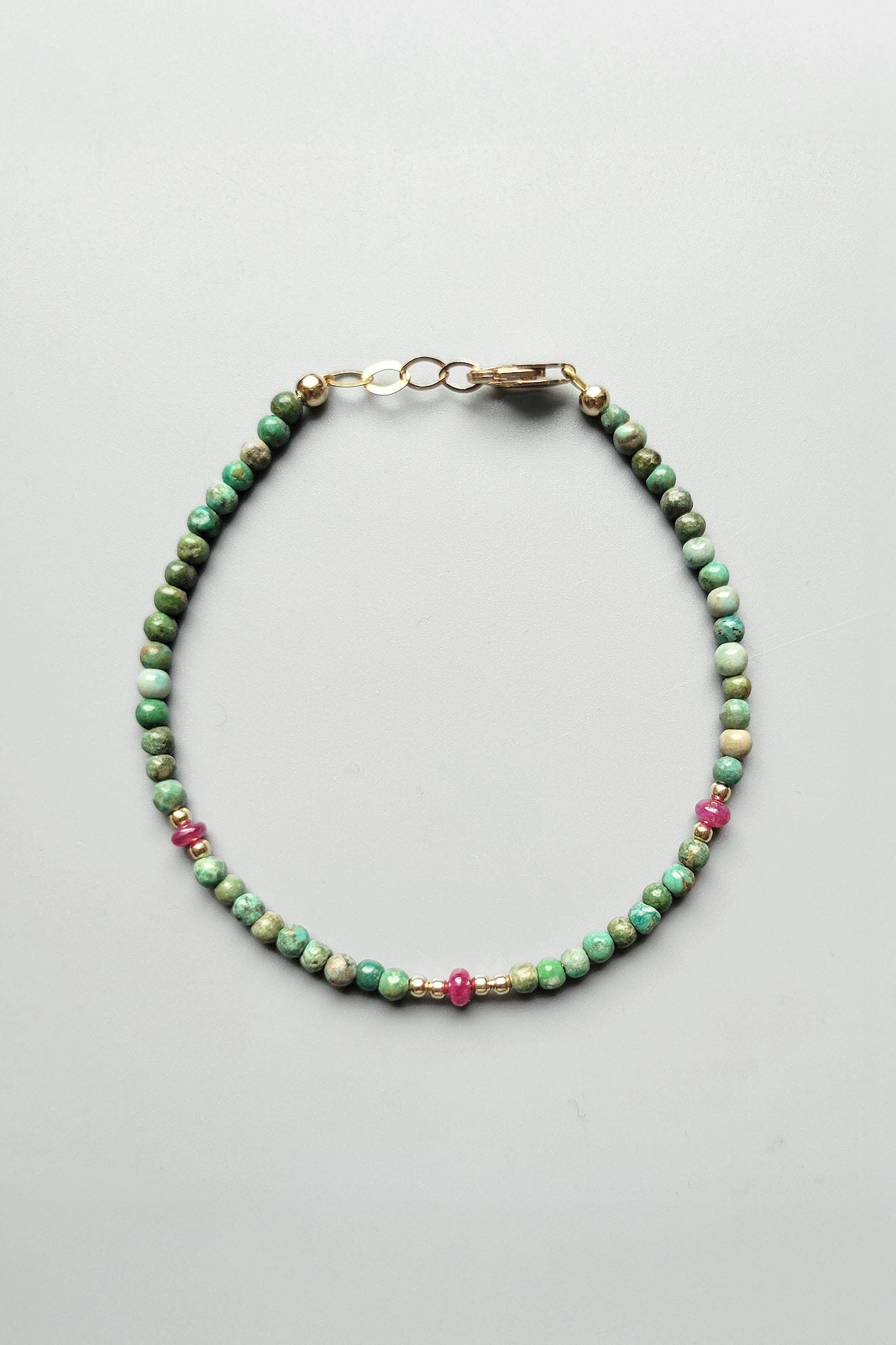 Beaded bracelet with green and pink beads on a gray background