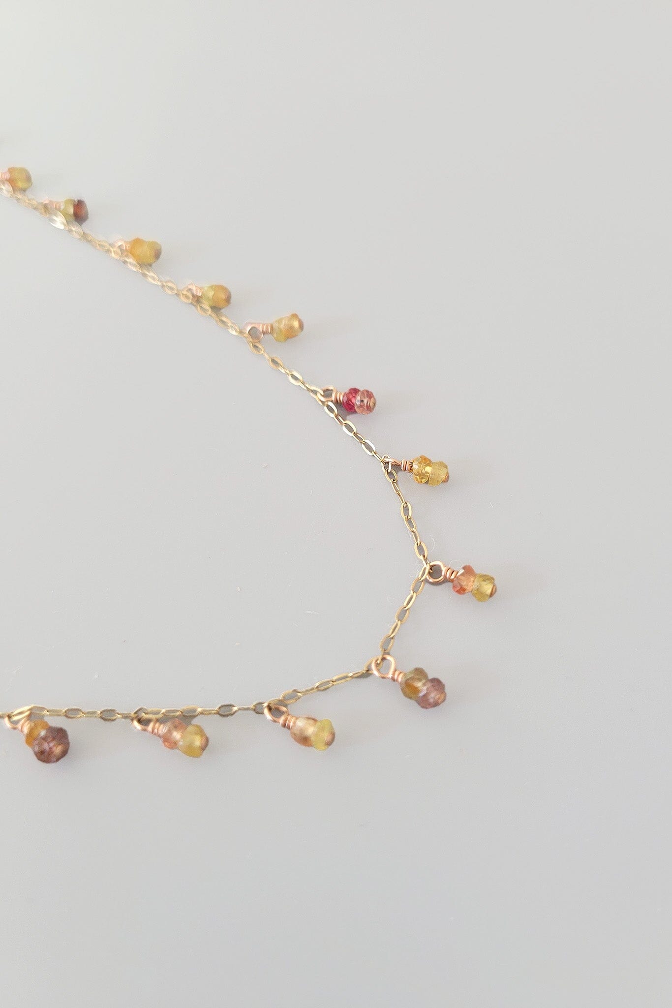 Delicate gold necklace with multicolored beads on a light gray background