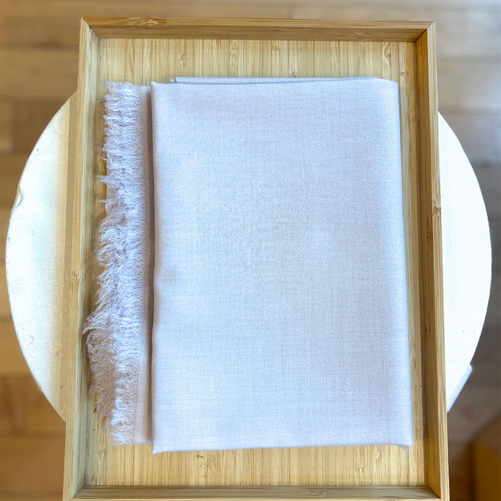 Folded silver cashmere scarf with frayed edge in a wooden frame on a wooden surface