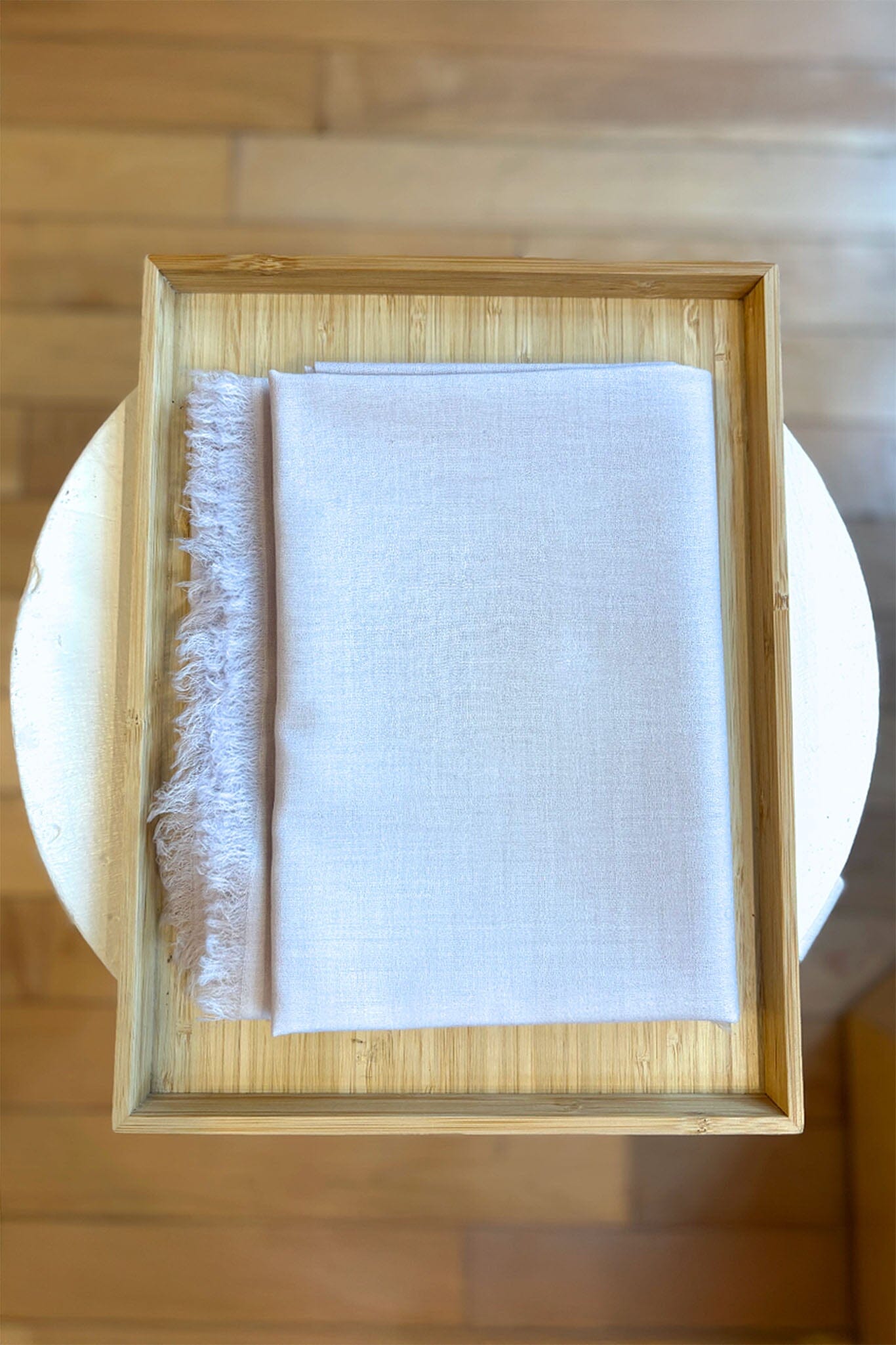 Folded silver cashmere scarf with frayed edge in a wooden frame on a wooden surface