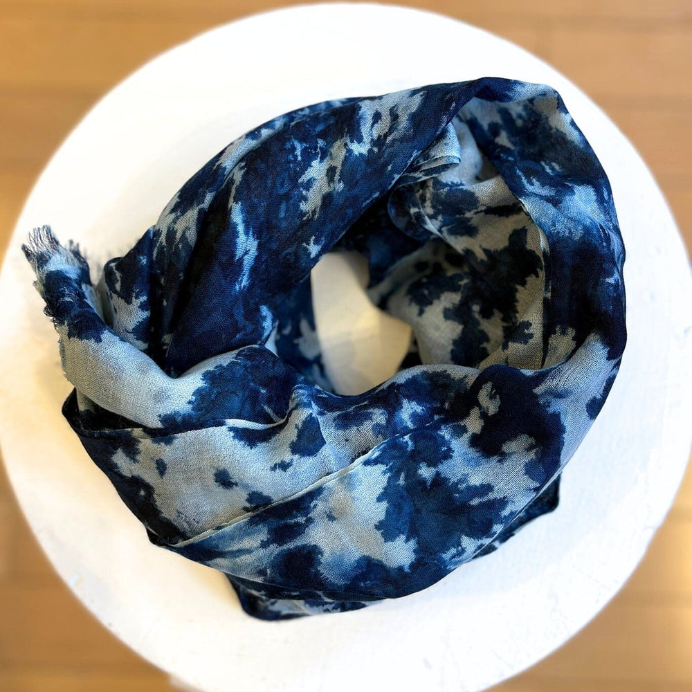Indigo blue and white patterned silk scarf on a white stand with a wooden background