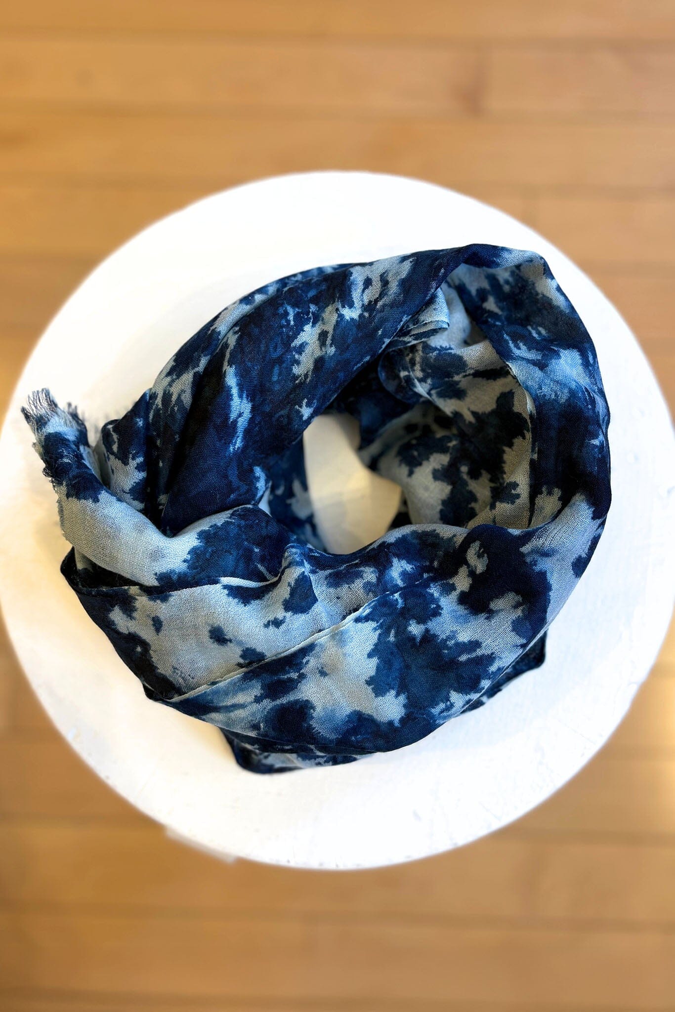 Indigo blue and white patterned silk scarf on a white stand with a wooden background