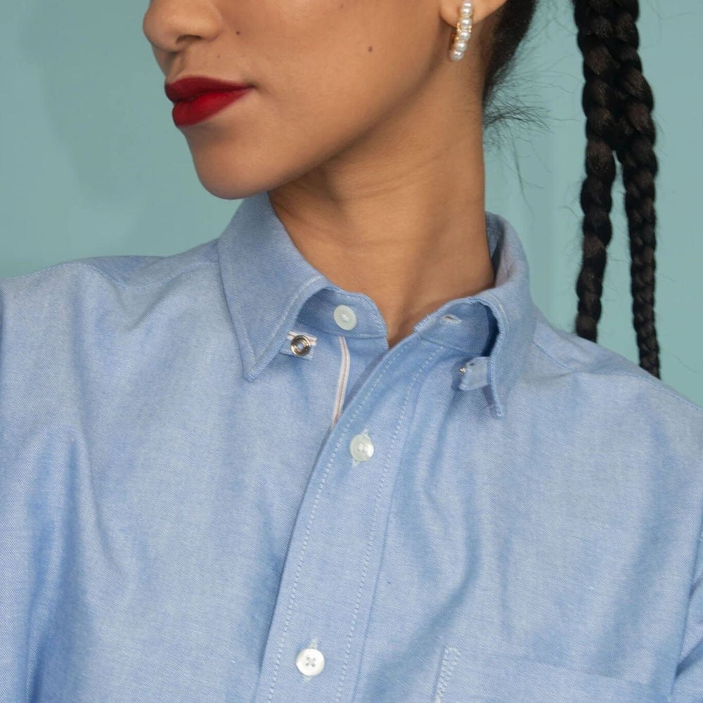 
                  
                    Woman wearing a light blue collared shirt with a plain background.
                  
                