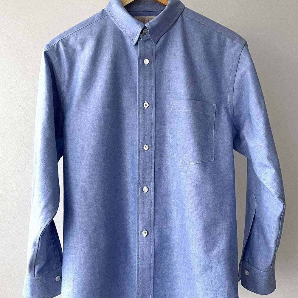
                  
                    Blue long sleeved shirt on a hanger against a plain background
                  
                