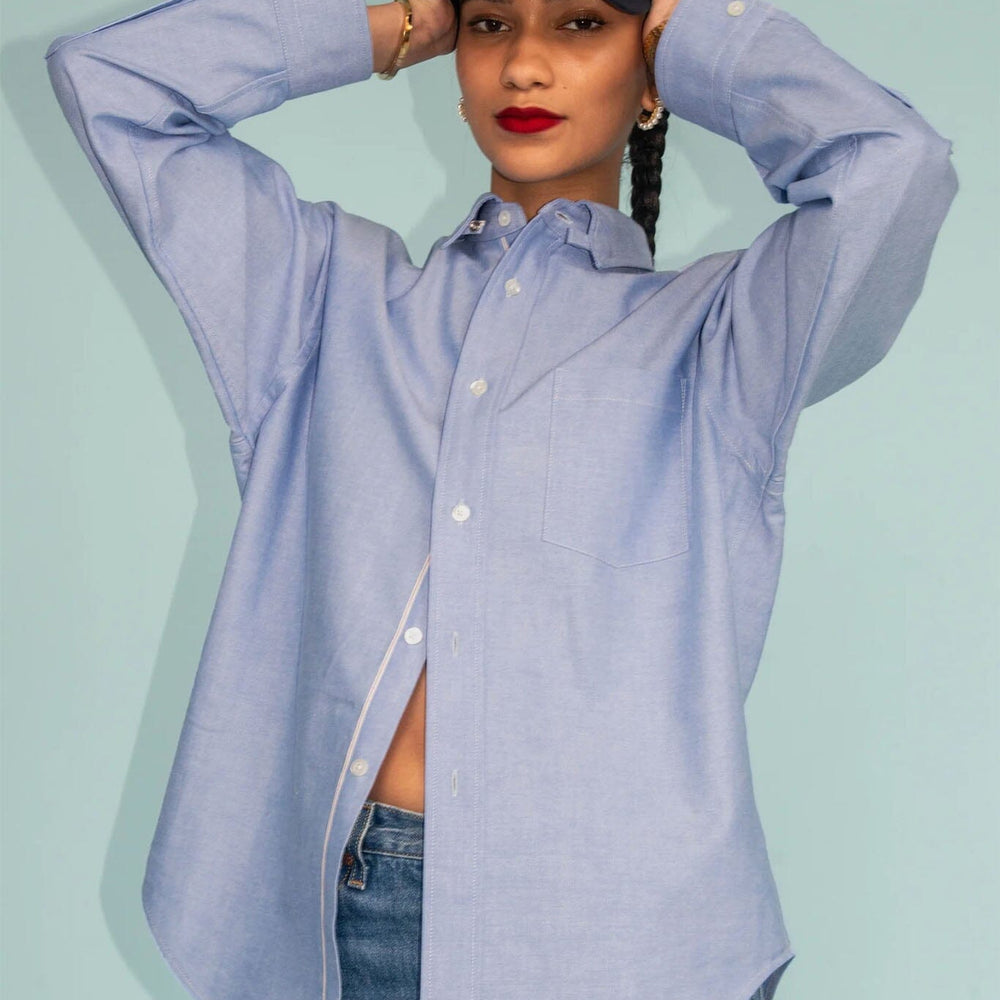 
                  
                    Person wearing a light blue button-up shirt and jeans with a black cap on a light blue background
                  
                