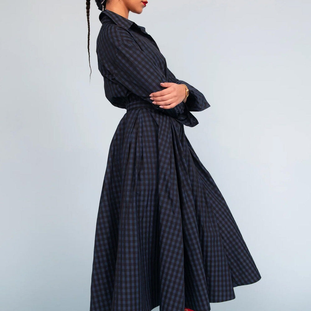 Woman wearing a dark checkered skirt with a head scarf against a light background