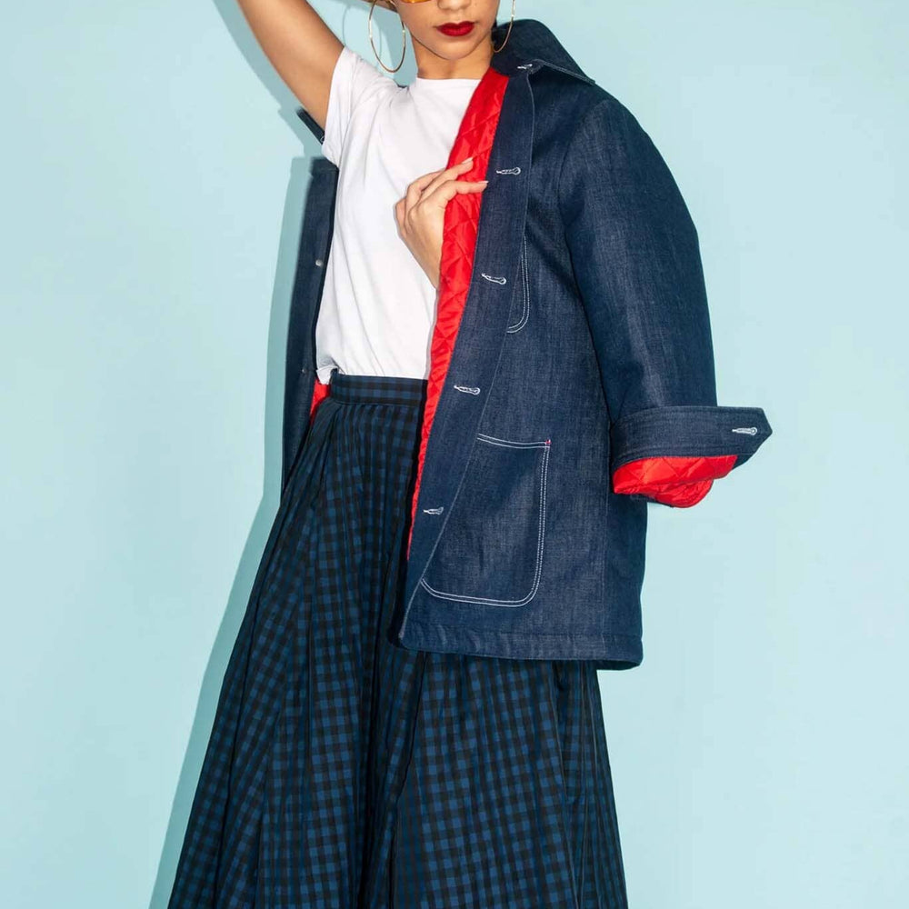 Person wearing a dark blue jacket with red lining and plaid skirt against a light blue background