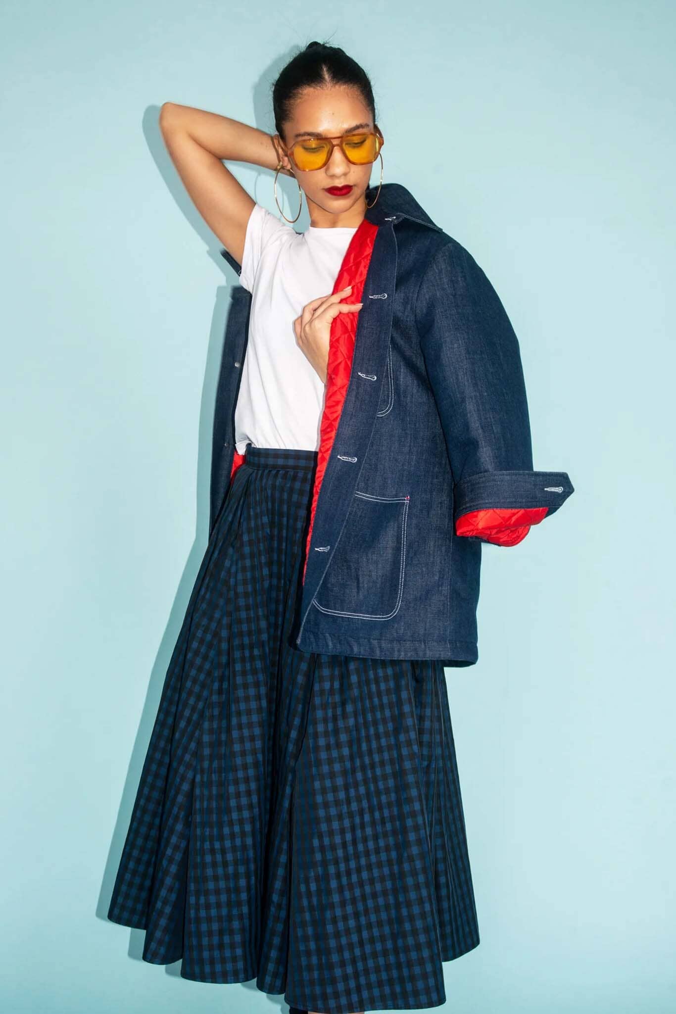 Person wearing a dark blue jacket with red lining and plaid skirt against a light blue background