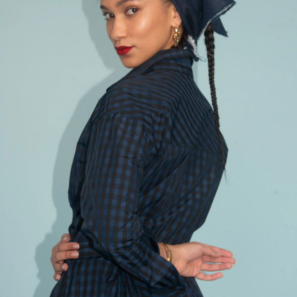 Woman wearing a dark blue checkered dress with a matching headscarf against a light blue background