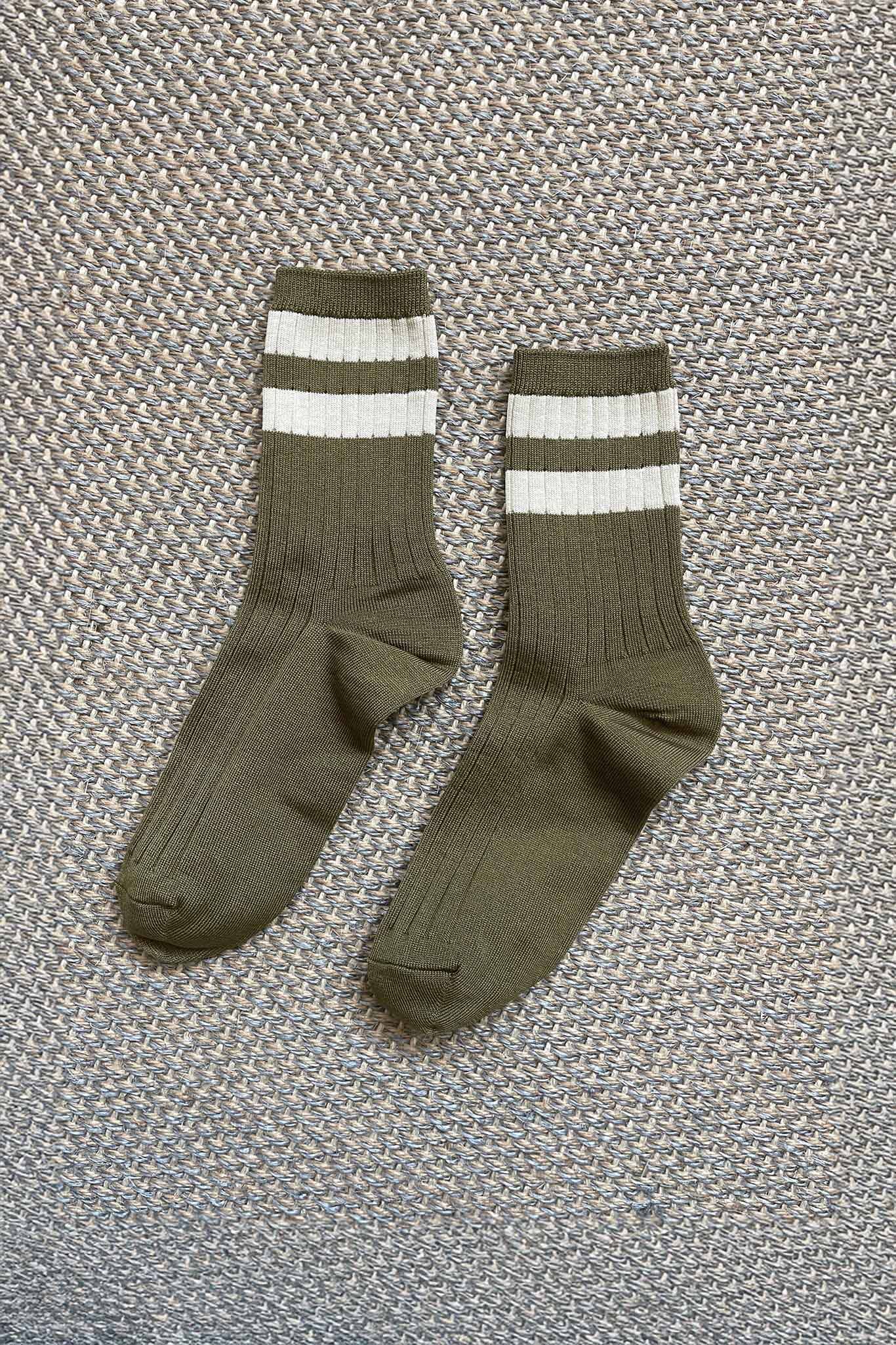 Pair of army green socks with white stripes on a textured gray background