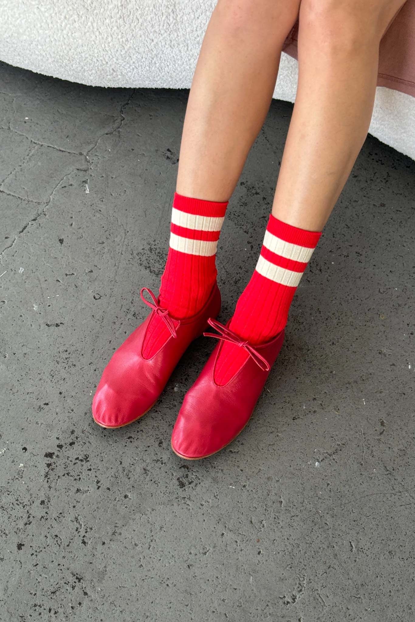 Red shoes and socks with white stripes on a gray pavement.