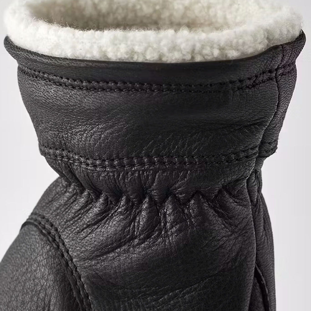 Close-up of a black leather glove with white fur lining on a light gray background