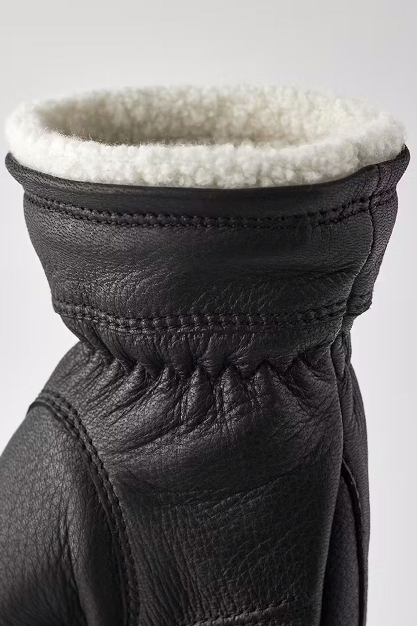 Close-up of a black leather glove with white fur lining on a light gray background