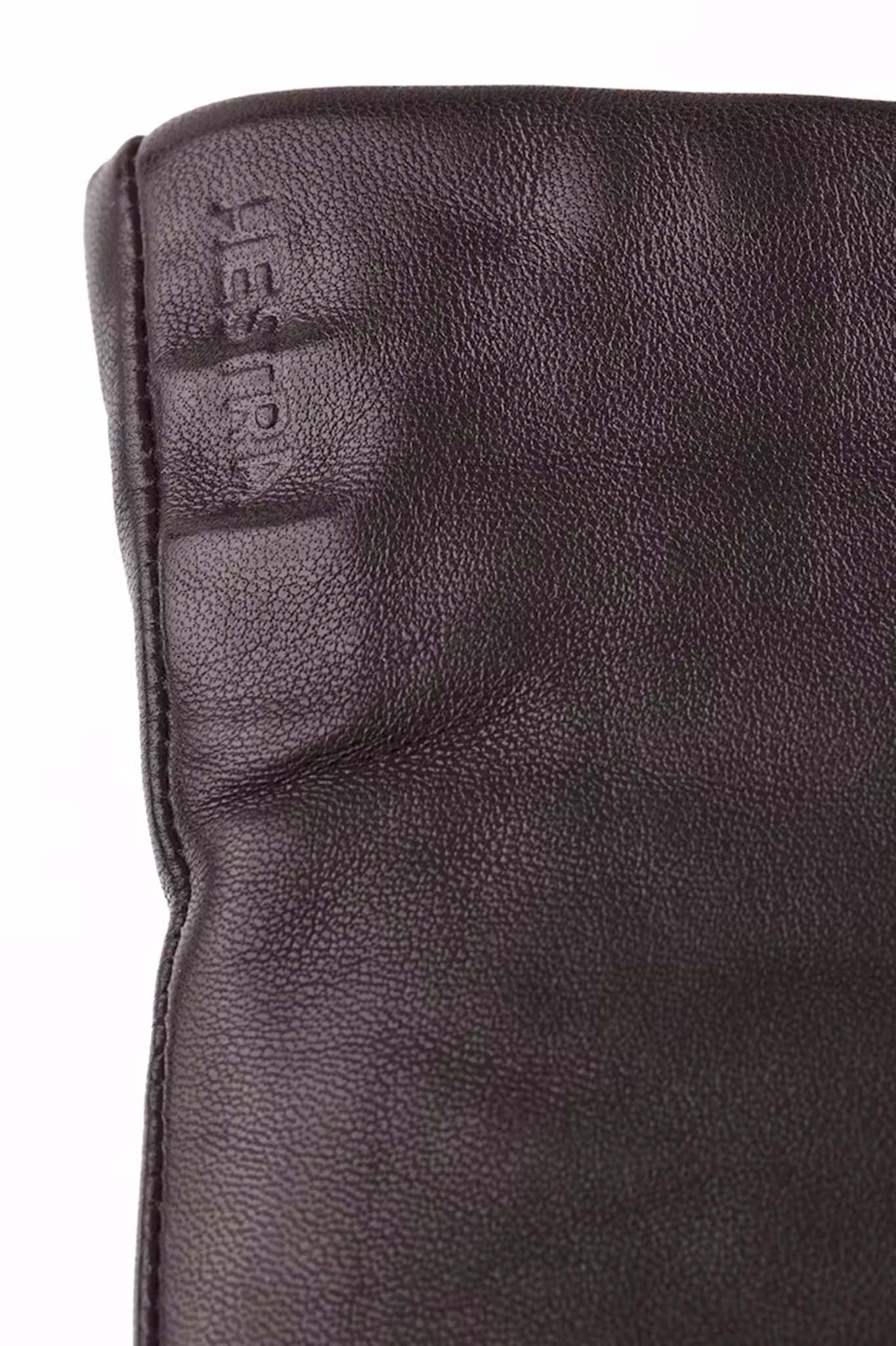 Close-up of a dark brown leather glove with 'Hestra' branding.