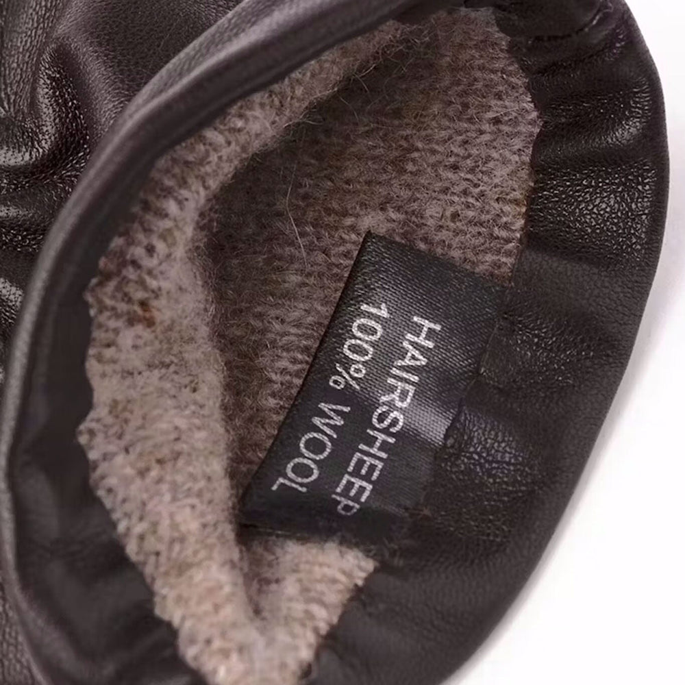
                  
                    Close-up of a black leather glove with gray shearling lining and a label indicating 100% wool.
                  
                
