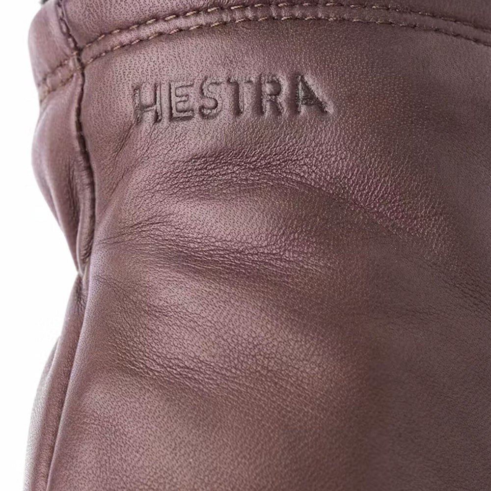 Close-up of brown leather glove with 'HESTRA' branding.