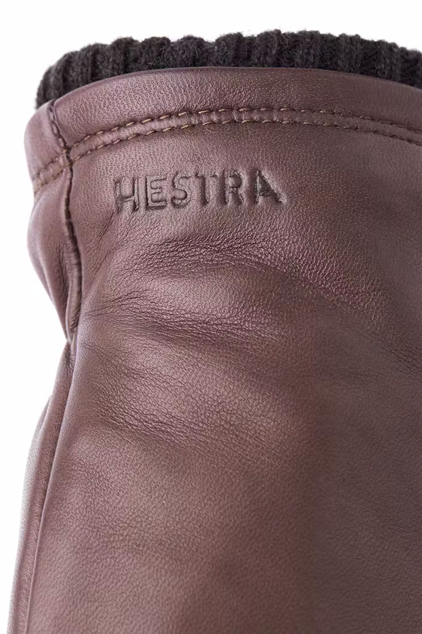 Close-up of brown leather glove with 'HESTRA' branding.