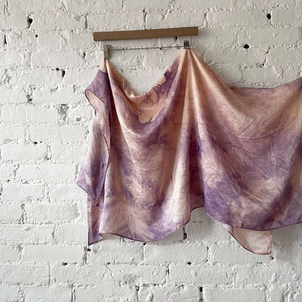 Purple and pink tie-dye silk scarf hanging against a white brick wall